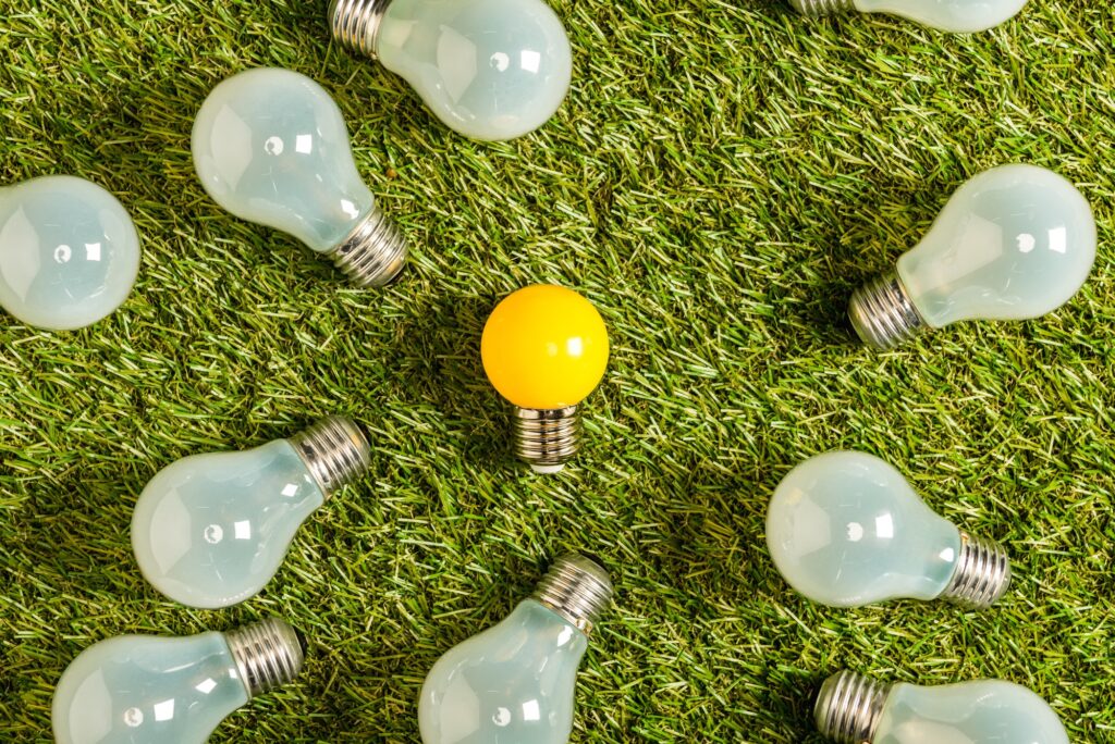 top view of fluorescent lamps near yellow lamp on green grass, energy efficiency concept